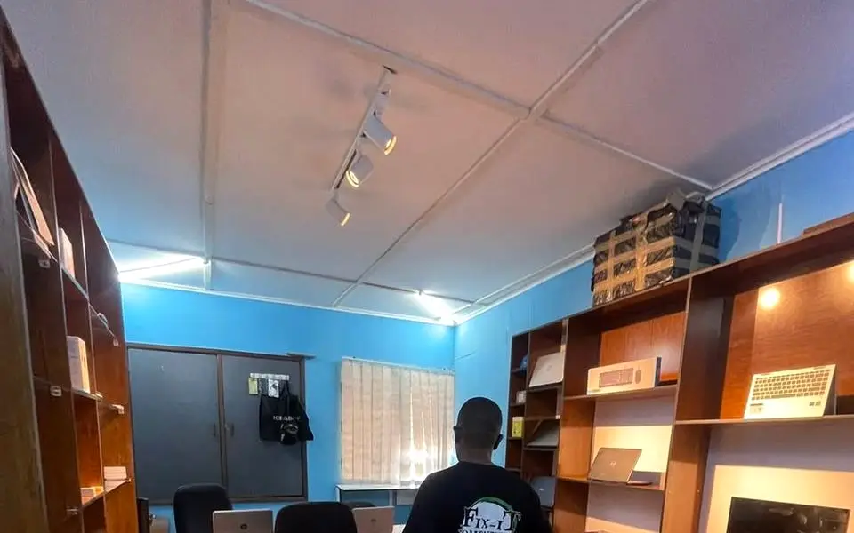 Inside the Fix-iT shop: blue walls, wooden shelving holding monitors, keyboards and receipt printers, with track lighting above.